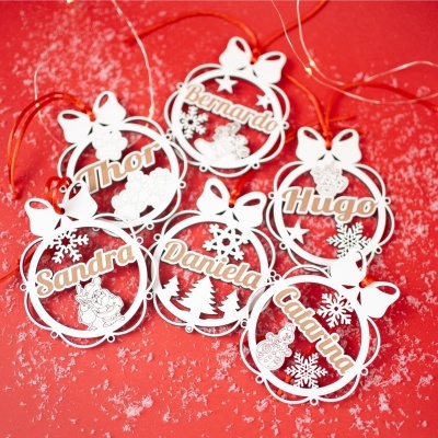 Etiquetas de Natal em acrílico branco com nomes e decorações sobre fundo vermelho com neve.