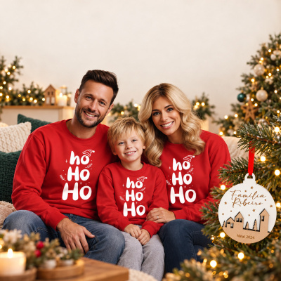 Família com camisolas vermelhas de Natal sentada junto a uma árvore decorada com luzes.
