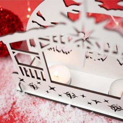 Suporte decorativo branco com recortes em forma de estrelas e velas acesas, em fundo vermelho com neve artificial.