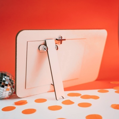 Parte traseira de monitor branco com suporte e confetes laranja em superfície branca, fundo laranja.