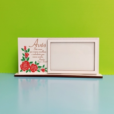 Porta-fotos branco decorado com rosas vermelhas e texto em português, sobre fundo verde e superfície azul.