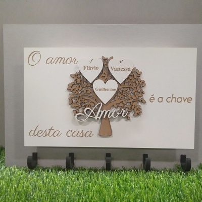 Quadro decorativo com árvore de madeira e corações com nomes em fundo branco e base cinza.