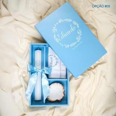 Caixa azul decorativa com vela, pano bordado e concha sobre fundo creme
