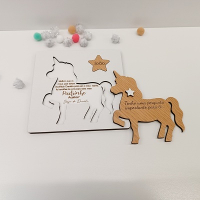 Tábua de unicórnio em madeira clara e branca com texto em português, estrela com nome João, e pompons coloridos ao redor