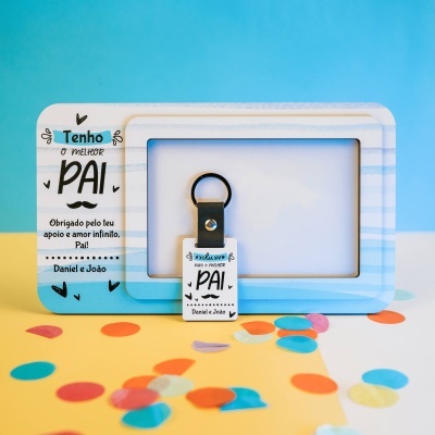 Chaveiro e moldura de quadro branco e azul com texto para pai e confetes coloridos no fundo.