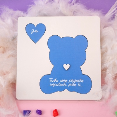 Cartão branco com recortes azuis de coração e urso e texto em português em fundo de plumas