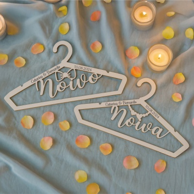 Cabides de madeira branca personalizados com nomes e data sobre tecido azul com pétalas e velas