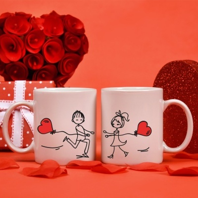 Duas canecas com ilustrações de casal e coração, presentes e decoração vermelha ao fundo