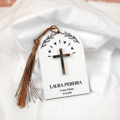 Etiqueta branca com cruz dourada e tassel castanho sobre tecido branco