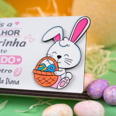 Cartão com desenho de coelho segurando cesta com ovos de Páscoa e ovos coloridos ao fundo