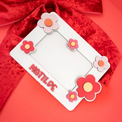 Moldura branca decorada com flores e nome MATILDE sobre fundo vermelho com laço de veludo