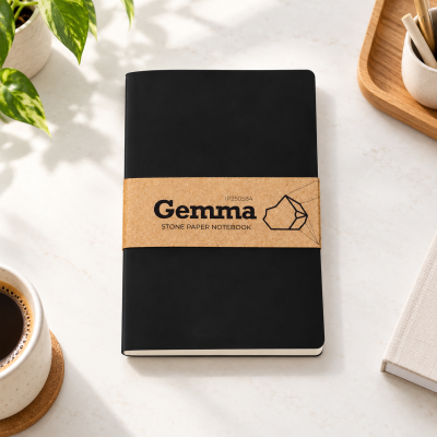 Caderno preto Gemma com faixa de papel e acessórios de escritório sobre mesa clara