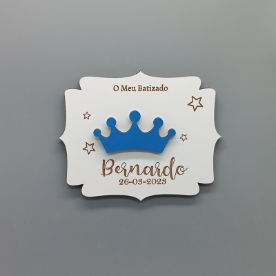 Placa decorativa branca com coroa azul e texto dourado para batizado.