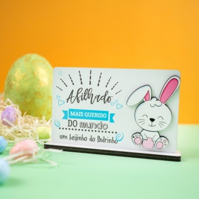 Cartão decorativo com coelho branco sorridente e texto em português com ovos coloridos ao fundo.