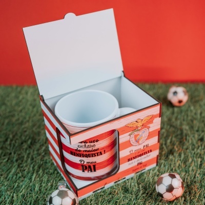 Caneca branca em embalagem vermelha e branca com texto em português e mini bolas de futebol no chão