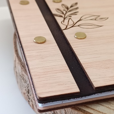 Caderno com capa de madeira clara e detalhes de folhas gravados.