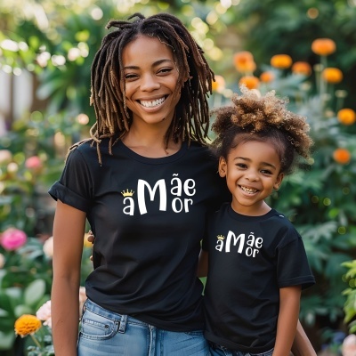 Mulher e criança com t-shirts pretas com texto branco e coroa amarela, em jardim com flores ao fundo