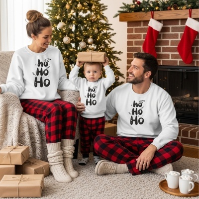 Família com pijamas de Natal brancos e calças vermelhas aos quadrados sentados perto de árvore de Natal e lareira com meias vermelhas.