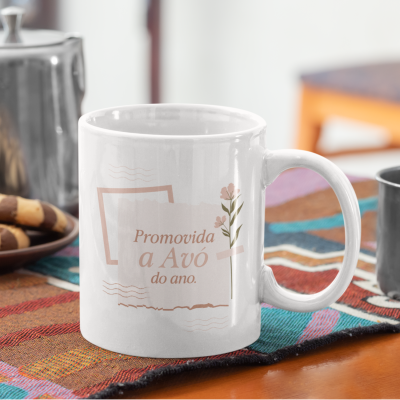 Caneca branca com texto Promovida a Avó do ano. e flores, sobre mesa com pano colorido