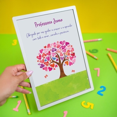 Tablet branco com imagem de árvore colorida de corações e nomes, em fundo amarelo e verde com objetos escolares