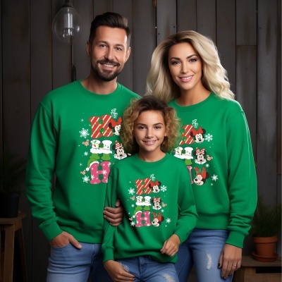 Três pessoas com sweatshirts verdes estampadas com Minnie Mouse e jeans azuis rasgados, em frente a parede de madeira cinza escura.