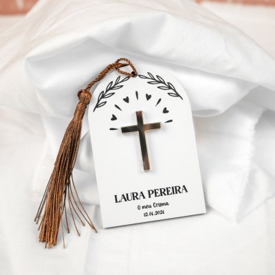 Etiqueta branca com cruz dourada e cordão tassel castanho sobre tecido branco
