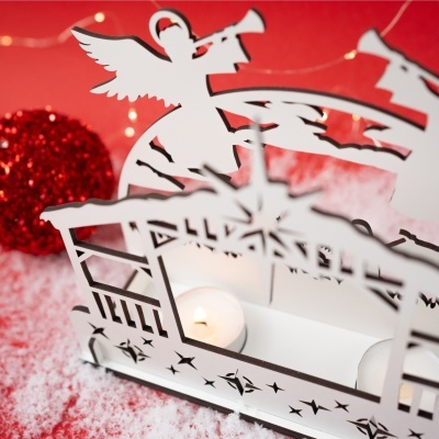 Castiçal branco com recortes de anjos e estrelas com vela acesa e decoração vermelha desfocada ao fundo