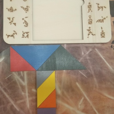 Tabuleiro de tangram em madeira com formas coloridas sobre tecido