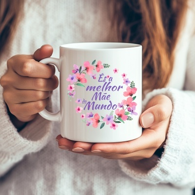 Caneca branca com flores rosas e lilás e texto És a melhor Mãe do Mundo sendo segurada por mãos femininas