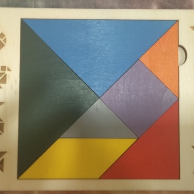 Tabuleiro de madeira para tangram com peças coloridas e recortes de figuras geométricas.
