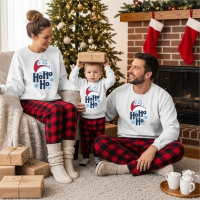 Família em pijamas de Natal com padrão xadrez e camisolas com texto Ho Ho Ho, junto a árvore e lareira decorada