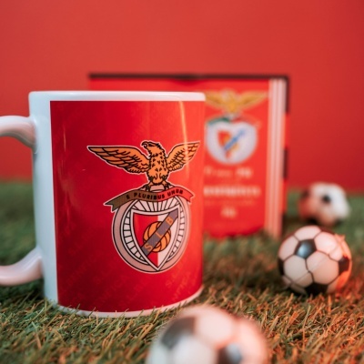 Caneca branca com emblema do SL Benfica sobre relva com mini bolas de futebol