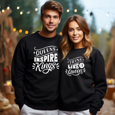 Casal com sweatshirts pretas com frases em branco e calças claras em ambiente externo com luzes desfocadas.