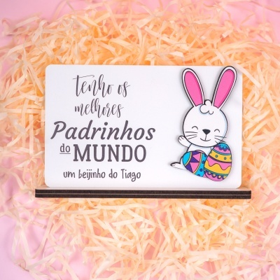 Placa com mensagem e figura de coelho com ovos coloridos num fundo de palha amarela