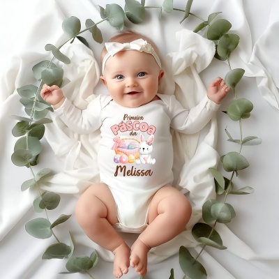 Bebé com body branco personalizado e banda de laço de cabeça, repousa em tecido branco rodeada de folhas verdes.