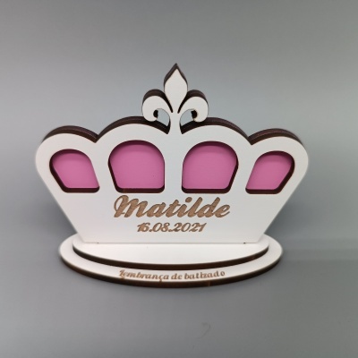 Objeto decorativo em madeira em forma de coroa com fundo rosa e texto Matilde 15.08.2021 e lembrança de batizado