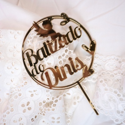 Decoração de bolo dourada com texto Baptizado do Daniel sobre tecido branco bordado