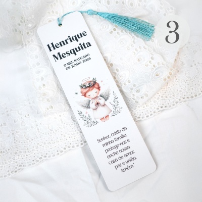 Marcador de página branco com anjo, tassel azul e texto, sobre tecido branco rendado com número 3