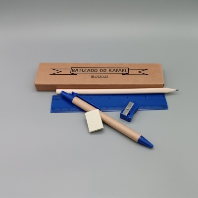 Conjunto de material escolar azul e branco com régua, compasso, apontador, lápis e borracha junto a caixa castanha com texto do batizado.