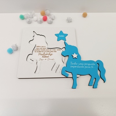 Convite em madeira azul em forma de unicórnio com pompons coloridos ao fundo