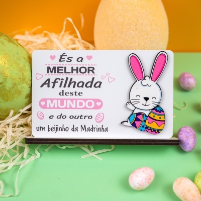 Placa de madeira com coelho e texto em português, decoração de páscoa com ovos coloridos e palha.