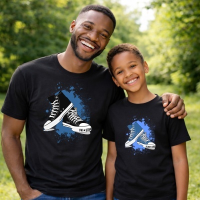 Duas pessoas usando t-shirts pretas com imagens de ténis e textos PAI STAR e FILHO STAR em ambiente verde exterior.