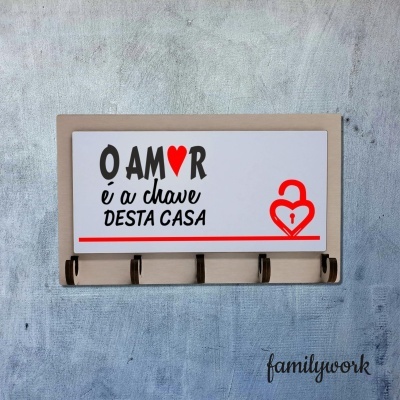 Suporte para chaves com texto decorativo sobre amor e chave, em madeira e com fundo branco, afixado numa parede cinza.