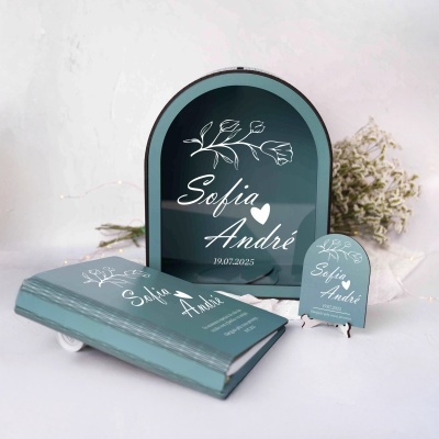 Livro, moldura e placa azul turquesa com nomes Sofia e André e data 19.07.2025 com flores ao fundo
