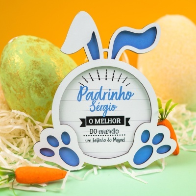 Placa decorativa em forma de coelho com texto para padrinho rodeada por cenouras e palha artificial