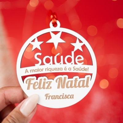 Etiqueta redonda branca com texto Feliz Natal e Saúde pendurada por cordão vermelho em fundo vermelho