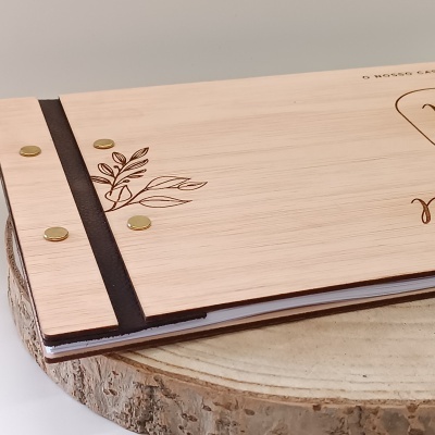 Livro ou caderno com capa de madeira clara decorada com desenho de folhas e parafusos dourados.