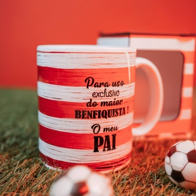 Caneca vermelha e branca com texto em frente, mini bolas de futebol e relva artificial ao redor