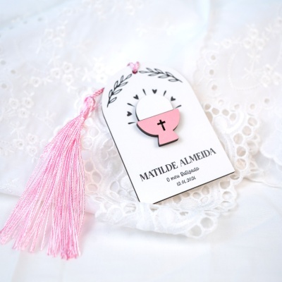 Etiqueta decorativa de batizado com franja cor-de-rosa sobre tecido branco decorado