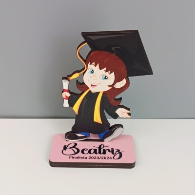 Estatueta de jovem com toga e capelo a segurar diploma sobre base com texto